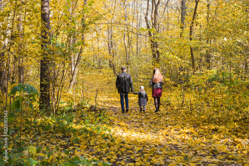 Fall, nature and family concept - family walking in autumn park, back view