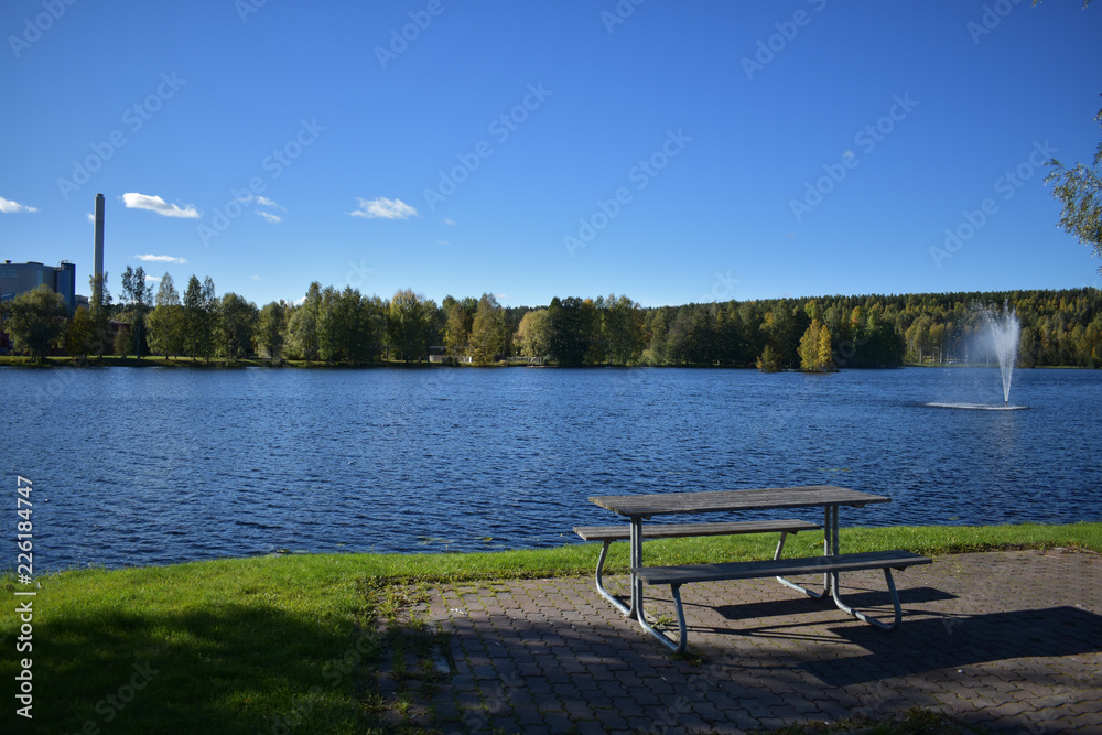 Relaxing blues and greens on a sunny day. The blue sky reflects its color to the lake which is surrounded by trees. A good place to sit, relax, and enjoy nature.
