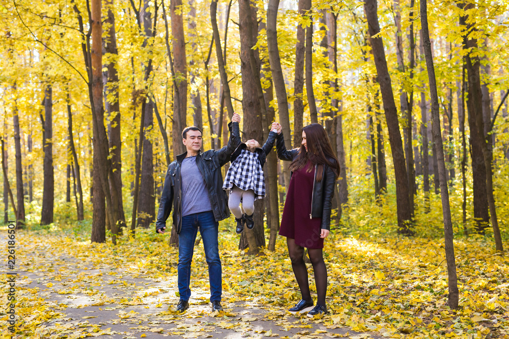 People, family and leisure concept - mixed race father and mother have fun in autumn park with their daughter People, family and leisure concept - mixed race father and mother have fun in autumn park with their daughter