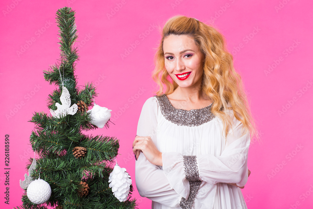Holidays concept - Blonde woman near christmas tree on pink background Holidays concept - Blonde woman near christmas tree on pink background