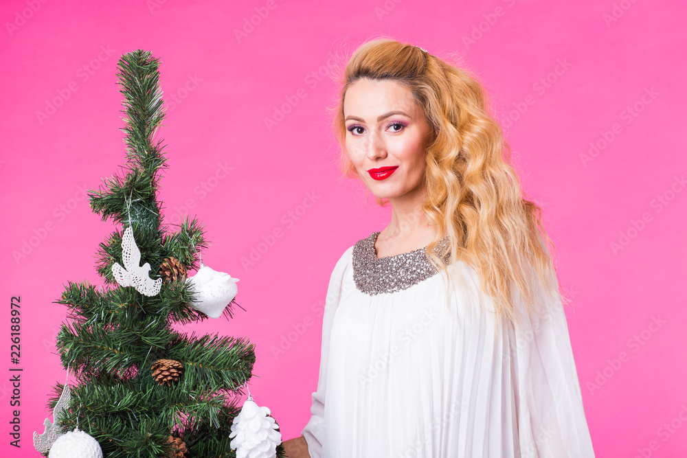 Holidays concept - Blonde woman near christmas tree on pink background Holidays concept - Blonde woman near christmas tree on pink background