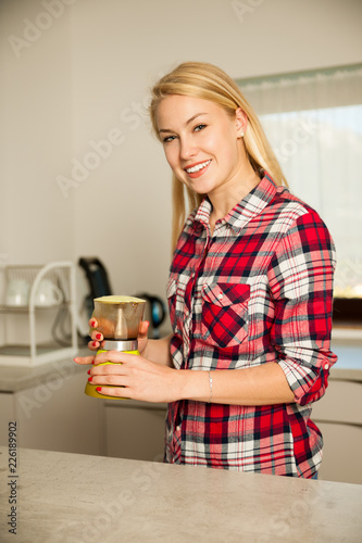 Beautiful young blond woman cooks coffee in kitchen