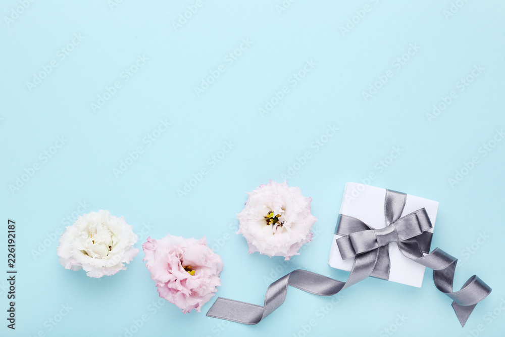 Gift box with ribbon and eustoma flowers on blue background