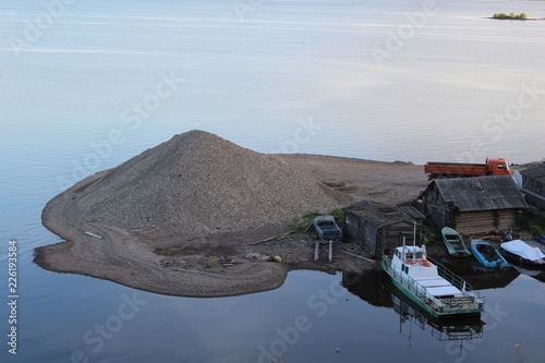 Island with a mountain of gravel among the river, and moored boats and boats. photo