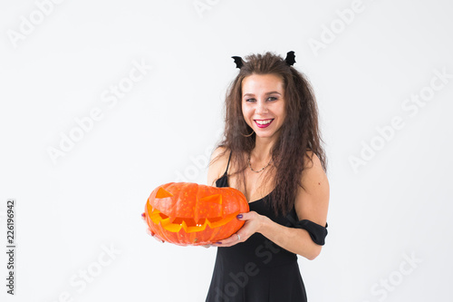 Excited happy young woman in halloween costume posing with carved pumpkin in lightroom