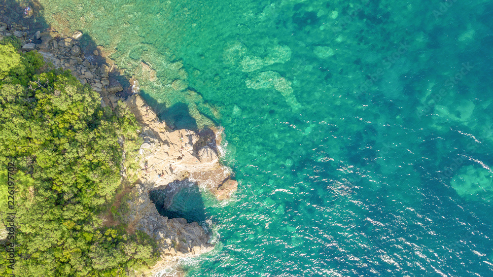 Top view aerial shot of tropical sea coast with beach, rocks, trees and blue water