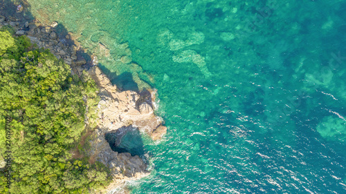 Top view aerial shot of tropical sea coast with beach, rocks, trees and blue water