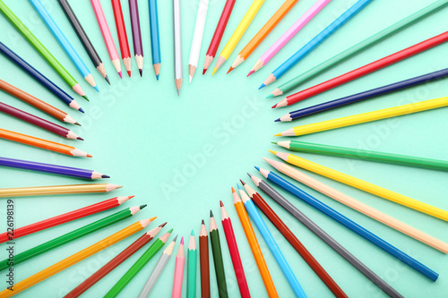 Colored pencils in heart shape on mint background