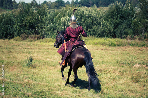 Medieval armored knight on horse from fantasy. Equestrian soldier in historical costume is in the summer field