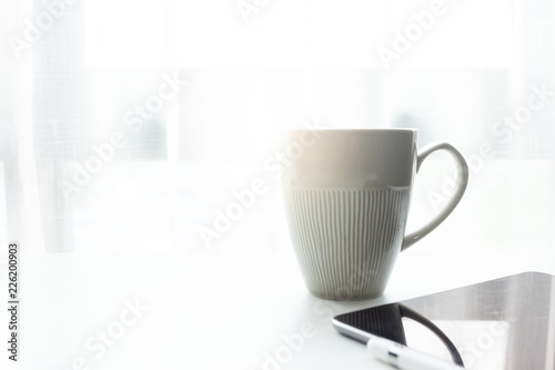 Coffee cup on white tablew with white window in the morning sunlight 