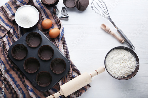 Empty cupcake cases with different kitchen utensils on wooden table