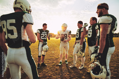 American football quarterback standing with his teammates discus photo