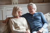 Happy loving senior couple talking looking in eyes relaxing on sofa together, elderly middle aged family embracing having fun enjoying conversation at home, smiling older man and woman good relation