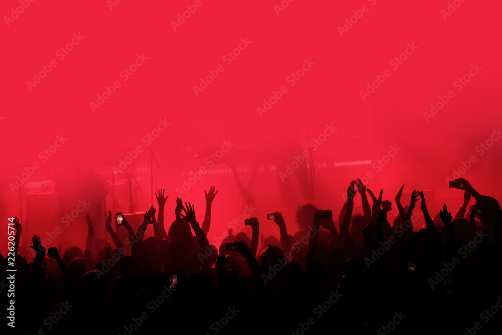 Red background with a crowd of cheering people at a concert. People with their hands up - obrazy, fototapety, plakaty 