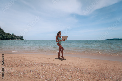 Young successful business woman or student in swimsuit using laptop in the beach. Working outdoors on seescape background. Mobile Office concept