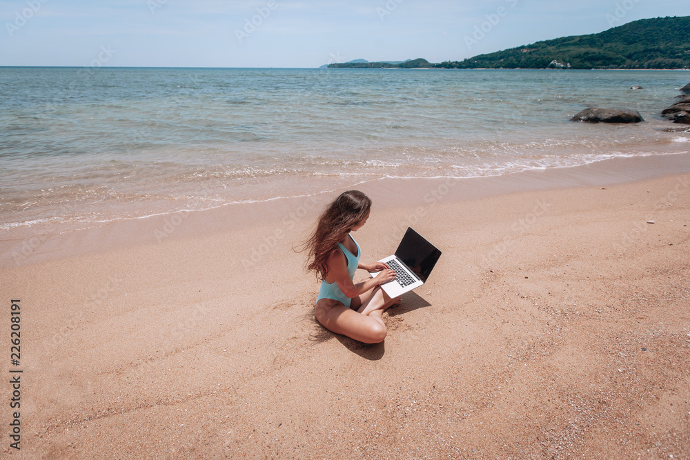 Young happy fitness yoga woman working with her laptop sitting on sitting on the sand, relaxing enjoy with nature. Young happy fitness yoga woman working with her laptop sitting on sitting on the sand, relaxing enjoy with nature.
