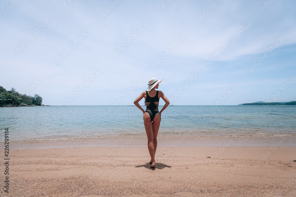 Summer lifestyle portrait of pretty young suntanned woman. Enjoying life on the beach of the tropical island. Wearing stylish bikini and wide brimmed hat with stripes. Looking at the sea Summer lifestyle portrait of pretty young suntanned woman. Enjoying life on the beach of the tropical island. Wearing stylish bikini and wide brimmed hat with stripes. Looking at the sea