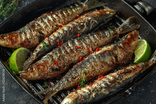 Grilled sardines with thyme, chili and lime wedges on cast iron skillet