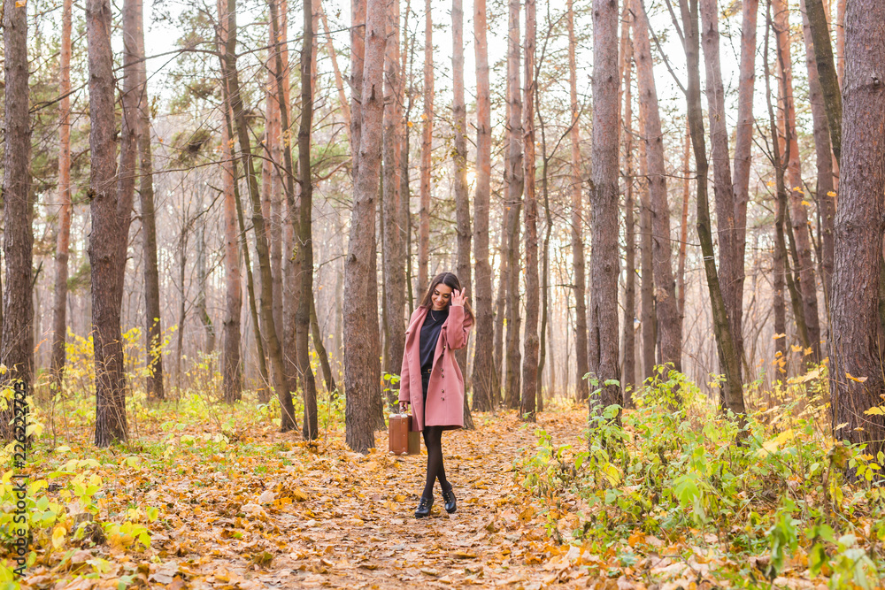 Autumn, nature and people concept - Portrait of beautiful smiling woman with brown suitcase walking in fall Autumn, nature and people concept - Portrait of beautiful smiling woman with brown suitcase walking in fall
