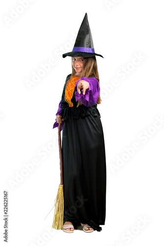 A full-length shot of a Little girl dressed as a witch for halloween holidays points finger at you isolated on white