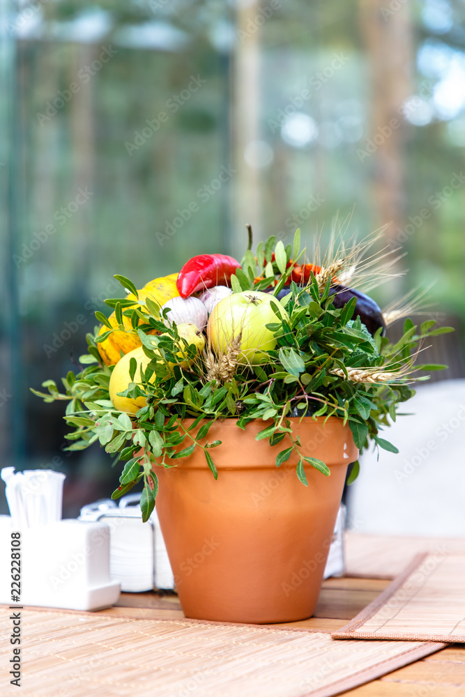 An unusual bouquet of fruits and vegetables in a ceramic pot is on the table