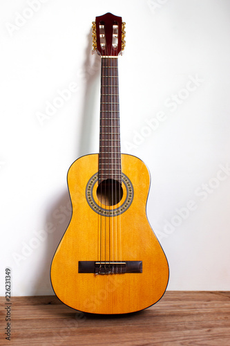 Classic guitar on wood floor with white wall. Favorite string music instrument.