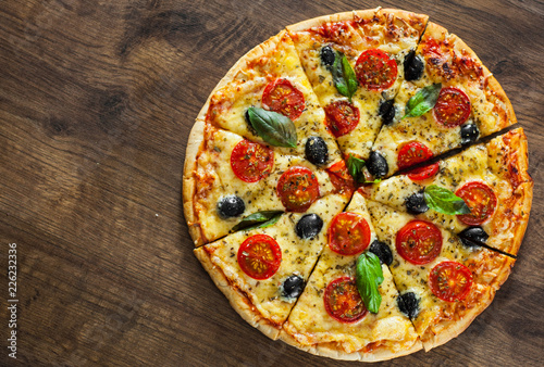 sliced Pizza Margherita or Margarita with Mozzarella cheese, tomato, olive. Italian pizza on wooden background