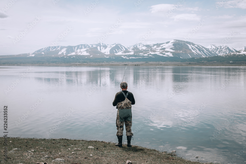 The guy fishing on the shore of a mountain lake . Reflection of mountains in water