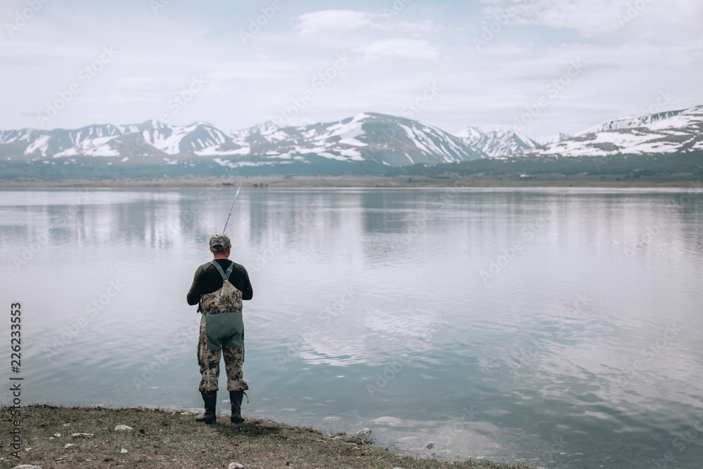 The guy fishing on the shore of a mountain lake . Reflection of mountains in water