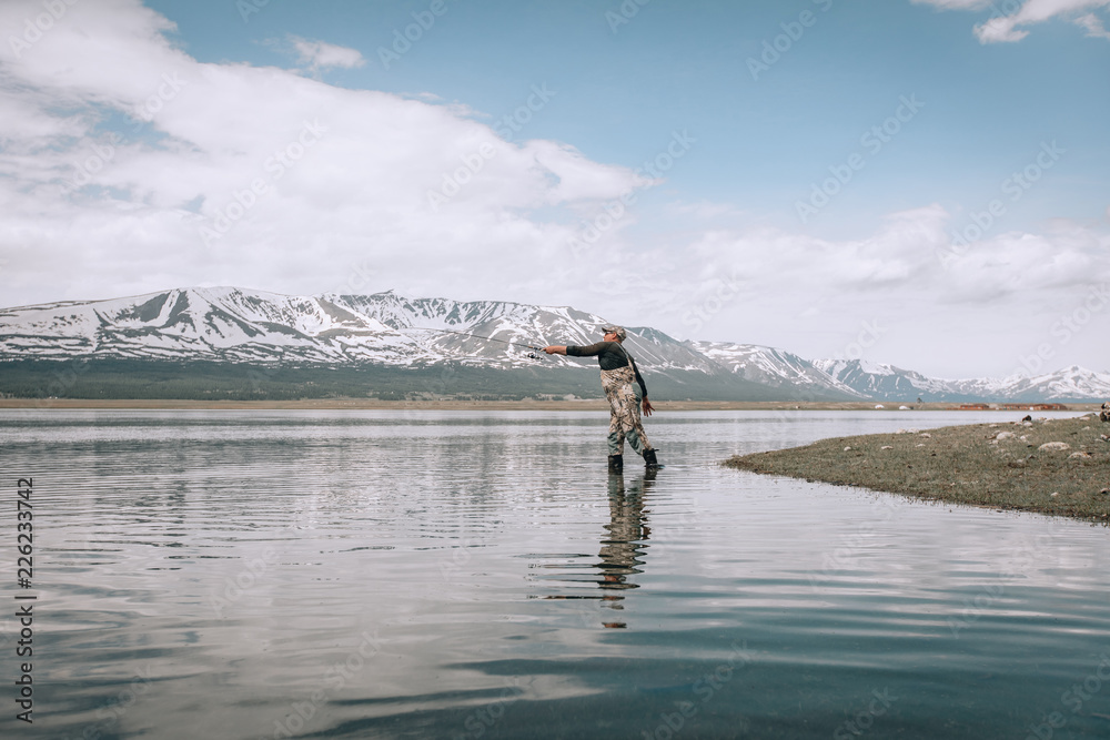Fototapeta premium The guy fishing on the shore of a mountain lake . Reflection of mountains in water