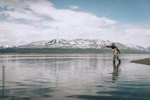 The guy fishing on the shore of a mountain lake . Reflection of mountains in water