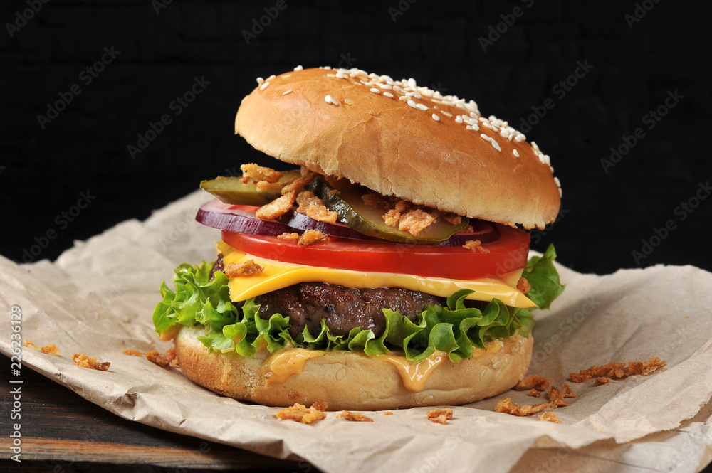 Cheeseburger on craft paper. Dried onions are scattered around the cheeseburger. Black background. Close-up. Macro shooting. Cheeseburger on craft paper. Dried onions are scattered around the cheeseburger. Black background. Close-up. Macro shooting.