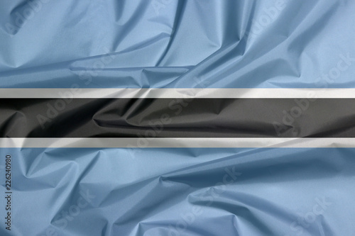 Fototapeta Naklejka Na Ścianę i Meble -  Fabric flag of Botswana. Crease of Botswana flag background, black stripe with a thin white frame on light blue.