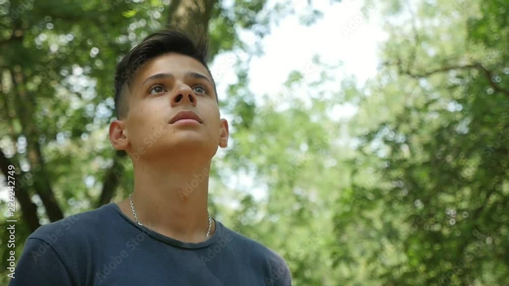 Down up view of a sportive young man with a crew haircut standing and looking confidently up in a leafy green wood on a sunny day Down up view of a sportive young man with a crew haircut standing and looking confidently up in a leafy green wood on a sunny day
