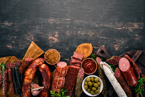 Assortment of salami and snacks. Sausage Fouet, sausages, salami, paperoni. On a black wooden background. Top view. Free space for your text. photo