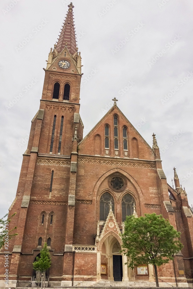Fototapeta premium Christian church with bell tower, christian church with red bricks on a cloudy sky background, clock tower with a spire
