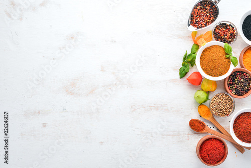 Fototapeta Naklejka Na Ścianę i Meble -  A set of Spices and herbs on a white wooden table. Basil, pepper, saffron, spices. Indian traditional cuisine. Top view. Free copy space.