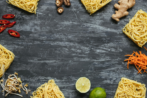 Ingredients for asian dish. Dried asian noodles with lime, nuts, cilantro and vegetables on wooden background