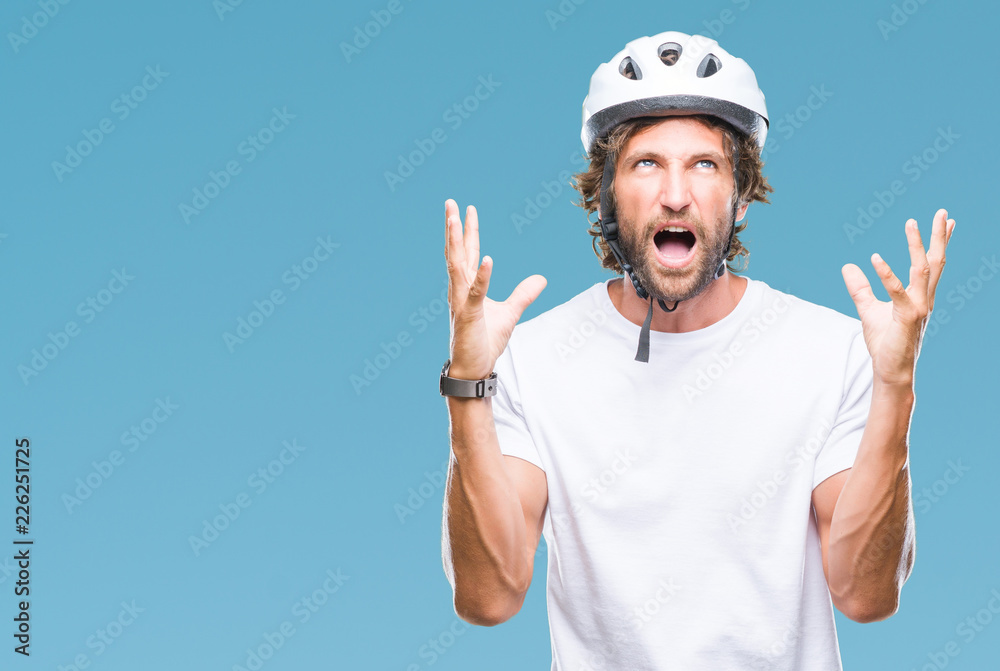 Naklejka premium Handsome hispanic cyclist man wearing safety helmet over isolated background crazy and mad shouting and yelling with aggressive expression and arms raised. Frustration concept.