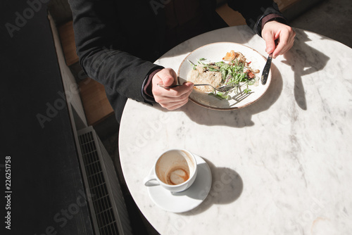 Сup of coffee and a plate of salad on the table. Man eats a salad with a fork and a knife in his hands. Top view. Healthy food. Lunch Break. Light and shadows. Copyspace