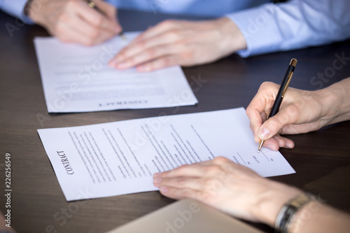 Close up view of male and female hands signing two contracts, man and woman put written signature on legal papers becoming new partners filling business document form promising good partnership deal photo