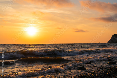 Minimalistic orange sunrise over the ocean with waves near the shore