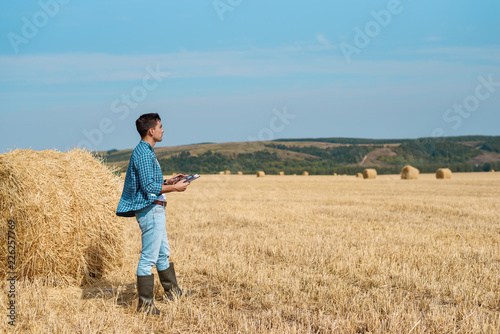 Agronomist farmer in jeans, shirt with a tablet is in the field with a stack, with tablet looking into the distance. Rural business, agricultural industry, freedom after work, concept © Руслан Галиуллин