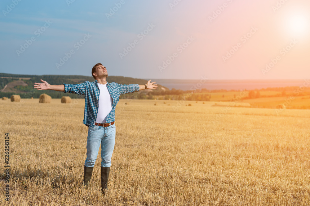 The guy in jeans, shirt, rubber boots in the field with his hands open, the concept of freedom, motivation, movement, a copy of space