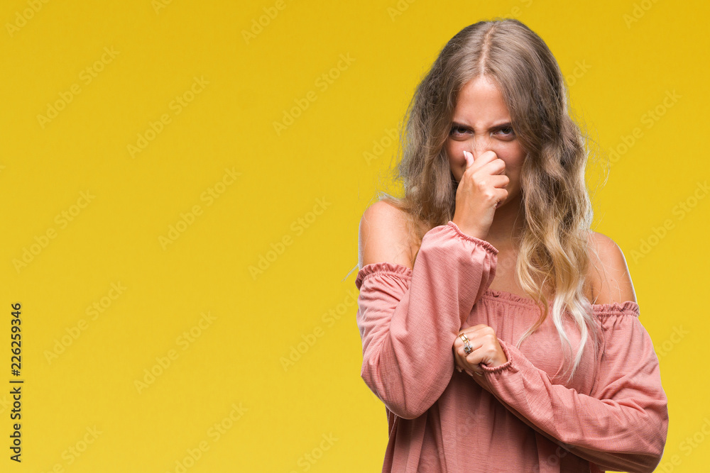 Beautiful young blonde woman over isolated background smelling something stinky and disgusting, intolerable smell, holding breath with fingers on nose. Bad smells concept.