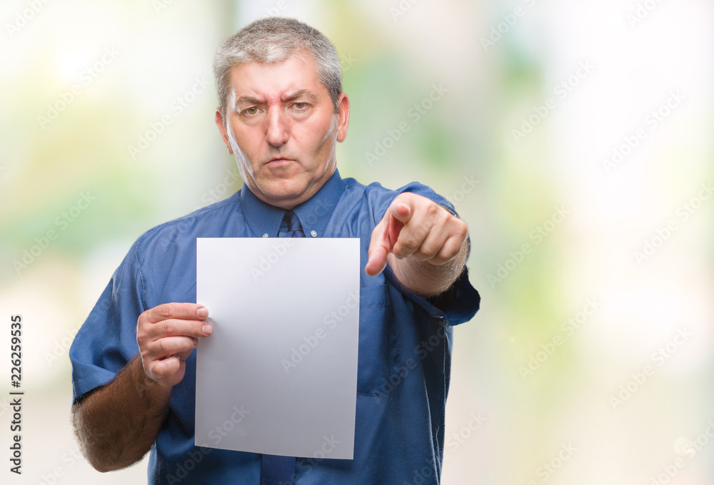 Handsome senior man holding blank sheet paper over isolated background pointing with finger to the camera and to you, hand sign, positive and confident gesture from the front Handsome senior man holding blank sheet paper over isolated background pointing with finger to the camera and to you, hand sign, positive and confident gesture from the front