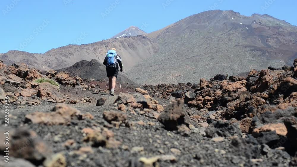 The tourist goes down the background of the volcanos Teide and Pico Viejo. Hiker man in beautiful mountain nature landscape. Canary Islands, Spain The tourist goes down the background of the volcanos Teide and Pico Viejo. Hiker man in beautiful mountain nature landscape. Canary Islands, Spain