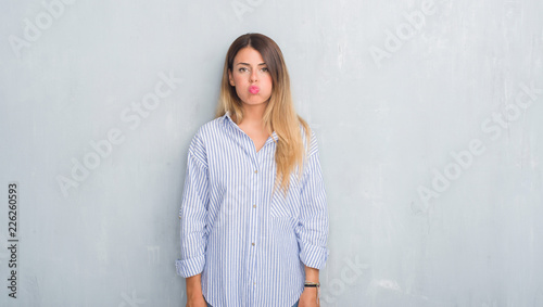 Young adult woman over grey grunge wall wearing fashion business outfit puffing cheeks with funny face. Mouth inflated with air, crazy expression. © Krakenimages.com