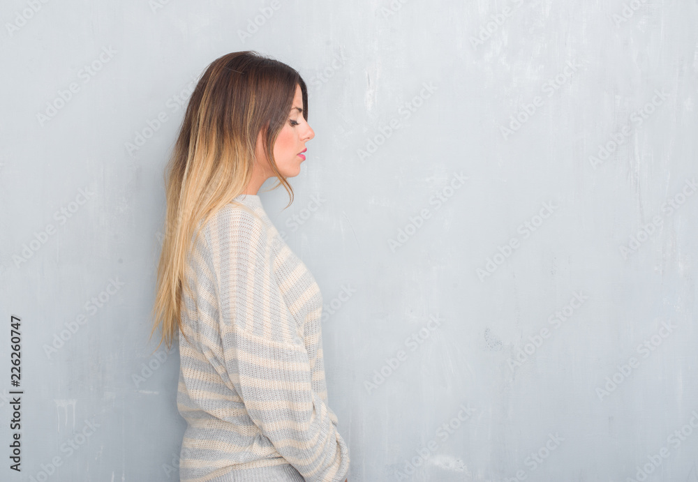 Young adult woman over grunge grey wall wearing winter sweater looking to side, relax profile pose with natural face with confident smile. Young adult woman over grunge grey wall wearing winter sweater looking to side, relax profile pose with natural face with confident smile.