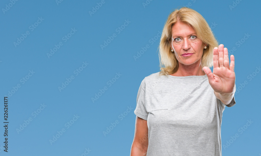 Fototapeta premium Middle age blonde woman over isolated background doing stop sing with palm of the hand. Warning expression with negative and serious gesture on the face.